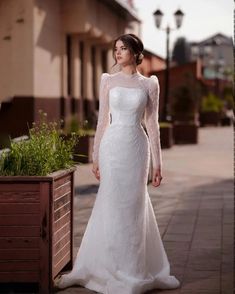 a woman in a white wedding dress standing next to a planter