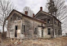 an old run down house sitting in the middle of a field next to some trees