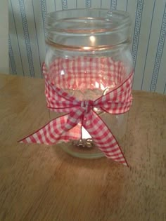 a glass jar with a red and white gingham bow on the lid sitting on a wooden table