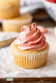 a cupcake with pink frosting sitting on top of paper