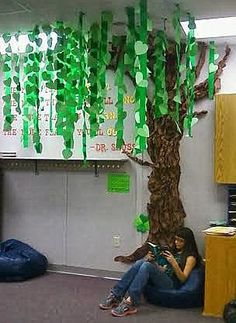 a woman is sitting under a tree with green paper streamers hanging from it's branches