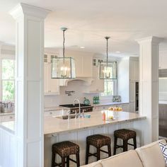 a living room and kitchen area in a house with white cabinets, counter tops, and bar stools