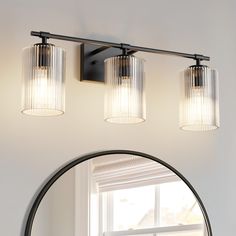 three light bathroom fixture with clear glass shades on the wall and round mirror above it