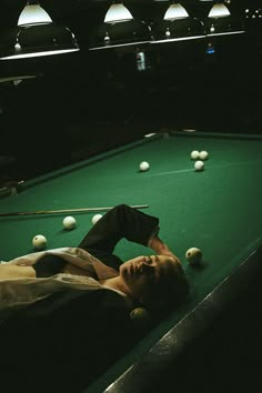 a man laying on top of a pool table next to a green billiarde