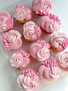 cupcakes with pink frosting are arranged in a plastic container on a table