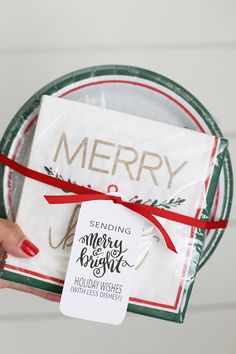 a person holding a christmas gift wrapped in white and red paper with a merry tag on it