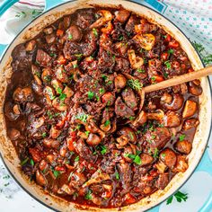 a large pot filled with meat and mushrooms on top of a blue table cloth next to utensils