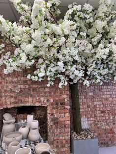 a tree with white flowers in front of a brick fireplace