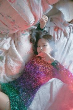 a woman laying on top of a bed next to a pillow covered in pink and green sequins