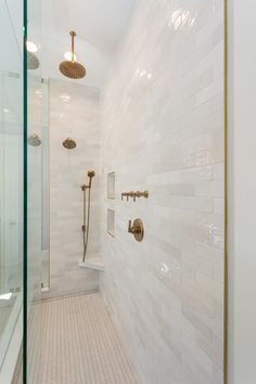 a walk in shower sitting next to a white tiled wall with gold fixtures on it