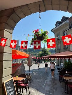 people are walking through an outdoor cafe with red and white flags hanging from the ceiling