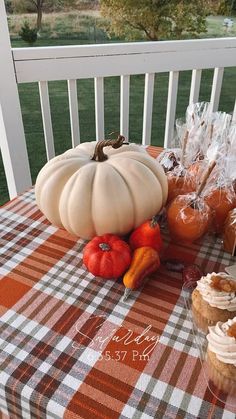 a table topped with cupcakes and pumpkins on top of a checkered table cloth