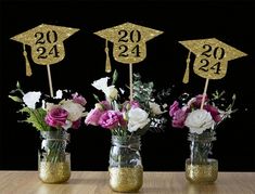 three mason jars filled with flowers and two graduation hats on top of each jar are decorated with gold glitter