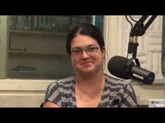 a woman with glasses is sitting in front of a microphone and smiling at the camera