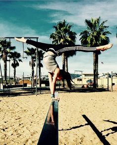 a woman doing a handstand on top of a metal rail in the sand