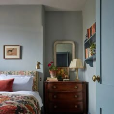 a bed sitting next to a dresser with a mirror on top of it and a lamp