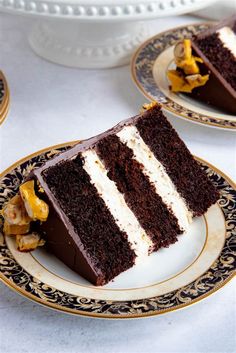 two slices of chocolate cake with white frosting on gold and black plates next to each other