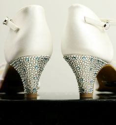 a pair of white high heels with blue and clear crystals on them, sitting on a black surface