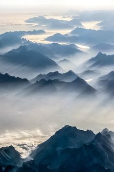 the view from an airplane looking down at mountains and valleys covered in foggy clouds