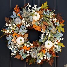 a wreath with white pumpkins and greenery is hanging on a black front door