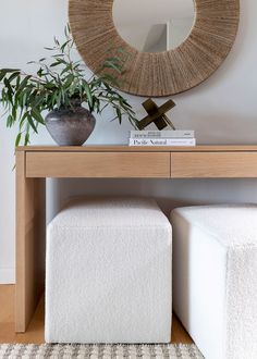 a white ottoman sitting under a mirror next to a potted plant on top of a wooden table