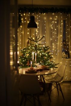 a dining room with a christmas tree in the corner and lights on the wall behind it