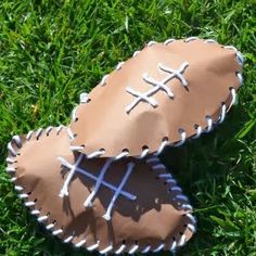 two baseball mitts sitting in the grass on top of each other, one with white stitching