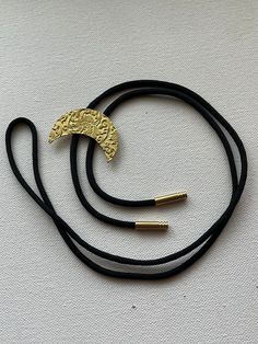 Bright yellow/gold brass crescent moon with floral pattern bolo tie necklace on black nylon cord. Adjustable Crescent Brass Jewelry, Bohemian Half Moon Adjustable Jewelry, Adjustable Bohemian Half Moon Jewelry, Adjustable Gold Lariat Necklace Choker, Adjustable Metal Crescent Necklace, Adjustable Crescent Metal Necklace, Elegant Adjustable Crescent Jewelry, Elegant Adjustable Crescent Shaped Jewelry, Adjustable Crescent Jewelry