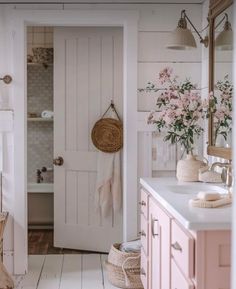 a white bathroom with pink cabinets and flowers in vases on the sink counter top