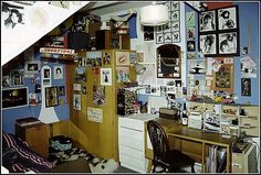 the room is cluttered with pictures and posters on the wall, along with a desk