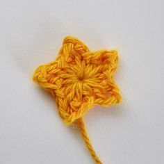 an orange crochet star on a white surface with yellow yarn in the shape of a flower