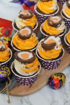 cupcakes are arranged on a wooden tray with chocolate eggs and candy candies