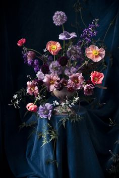 an arrangement of flowers in a vase on a blue table cloth with dark background,