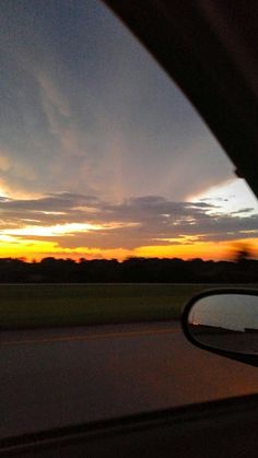 the sun is setting in the distance as seen from inside a car's side view mirror