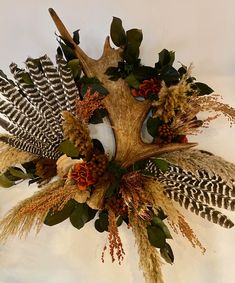 a wreath with feathers, flowers and leaves hanging on a wall in front of a white background