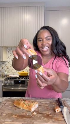 a woman is holding up a piece of pizza on a cutting board in the kitchen