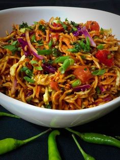 a white bowl filled with noodles and vegetables on top of a black table next to green peppers