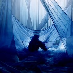 a person sitting on a bed in a room with blue sheets and drapes covering it