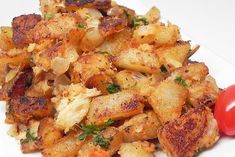 a white plate topped with fried potatoes and tomatoes next to a cherry tomato on the side