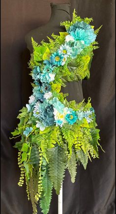 a mannequin is decorated with blue and green flowers, ferns and fern leaves