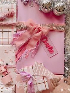 pink and silver wrapping paper with bows, ribbons, and other items on it next to christmas decorations