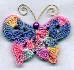 a colorful crocheted butterfly is hanging on a metal rack with a purple bead in the center