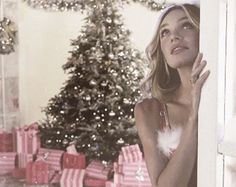 a woman leaning against a wall in front of a christmas tree