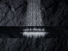 a black and white photo of water falling from a shower head in front of a rock wall