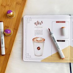 a desk with a calendar, pen and markers on it next to a cup of coffee