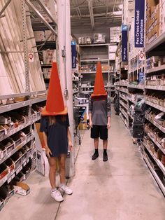 two people with orange cones on their heads walk down the aisle in a grocery store