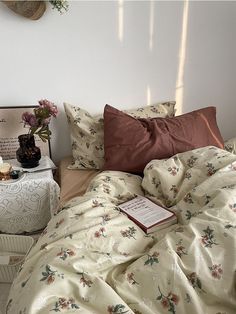 an unmade bed with flowers on it next to a table and lamp in the corner