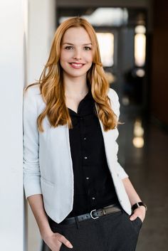 a woman standing next to a wall with her hands in her pockets and looking at the camera