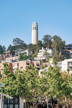 a tall clock tower towering over a city filled with trees and buildings on top of a hill