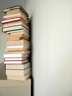 a stack of books sitting on top of a wooden shelf next to a white wall